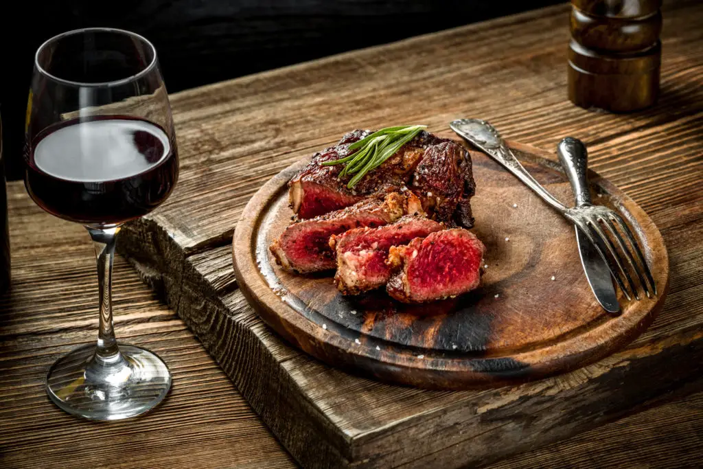 Discover the best wine with steak. The image shows grilled ribeye beef steak with red wine, herbs and spices.